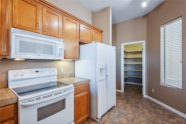 kitchen with white appliances, baseboards, brown cabinetry, and dark tile patterned flooring