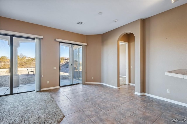 tiled spare room with baseboards, visible vents, arched walkways, and a wealth of natural light