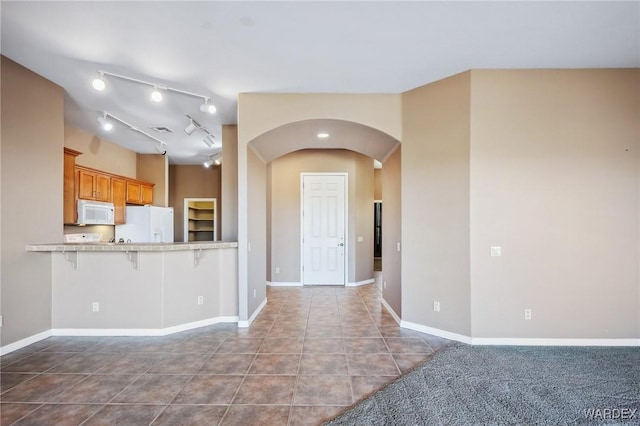 kitchen with arched walkways, a breakfast bar area, white appliances, dark tile patterned flooring, and light countertops