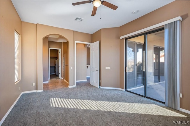 unfurnished bedroom featuring access to exterior, arched walkways, visible vents, light carpet, and baseboards