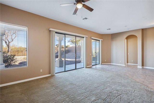 spare room with light colored carpet, arched walkways, a healthy amount of sunlight, and baseboards