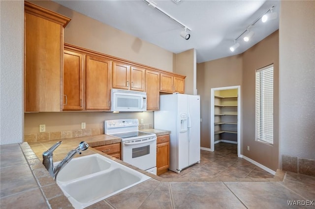 kitchen with light tile patterned floors, tile counters, brown cabinetry, a sink, and white appliances