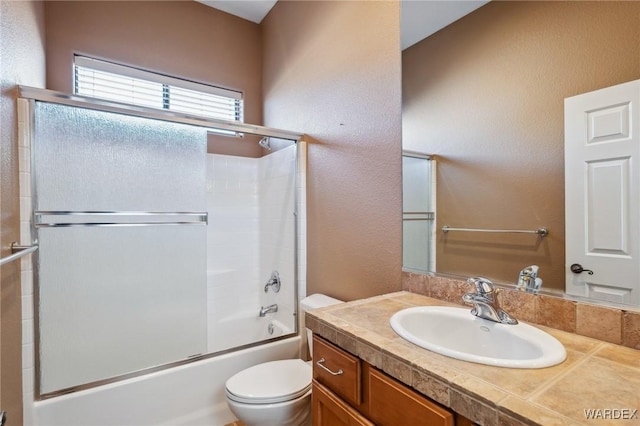 bathroom featuring a textured wall, bath / shower combo with glass door, vanity, and toilet