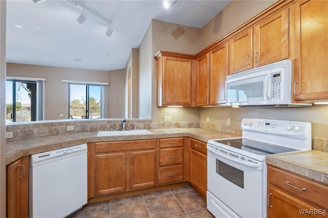 kitchen featuring white appliances, brown cabinetry, a sink, and tile counters