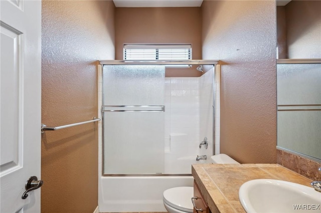 bathroom with combined bath / shower with glass door, a textured wall, vanity, and toilet