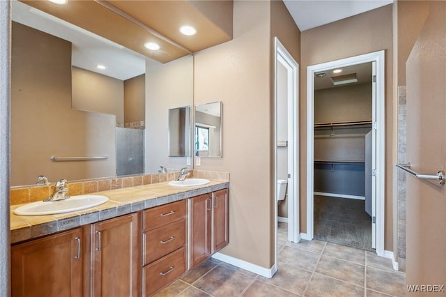 full bathroom featuring double vanity, a walk in closet, a sink, and tile patterned floors