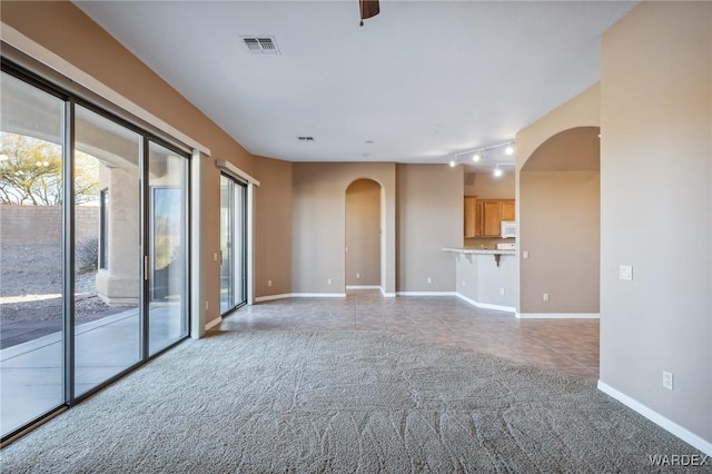 unfurnished living room with visible vents, arched walkways, baseboards, carpet, and tile patterned flooring