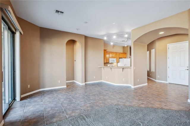 unfurnished living room featuring arched walkways, visible vents, baseboards, and dark tile patterned flooring