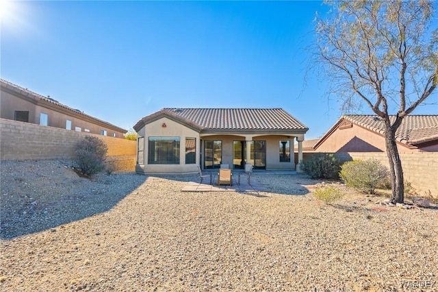 rear view of property featuring a tile roof, a fenced backyard, and stucco siding