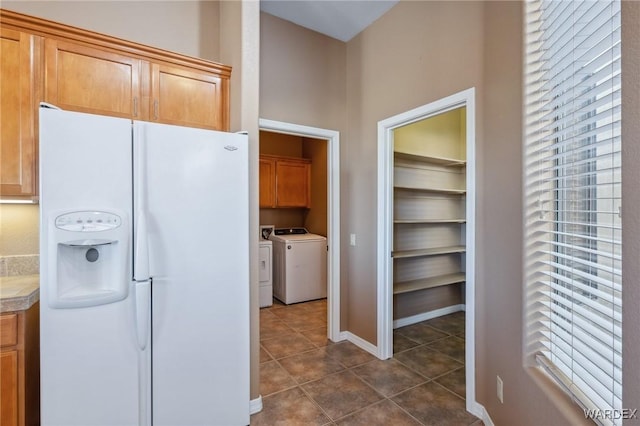 kitchen featuring white fridge with ice dispenser, dark tile patterned flooring, independent washer and dryer, and baseboards