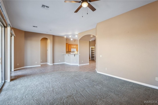 unfurnished living room with arched walkways, baseboards, visible vents, and light colored carpet