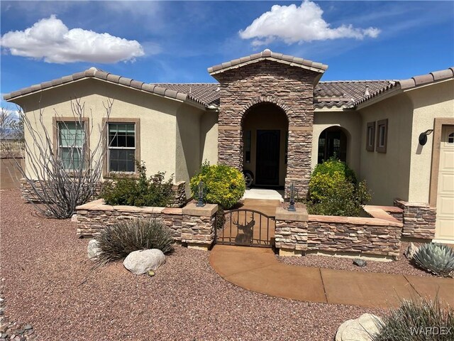 mediterranean / spanish home featuring stone siding, a tiled roof, a gate, and stucco siding