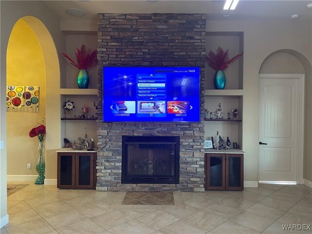 living area featuring built in features, arched walkways, a stone fireplace, and baseboards