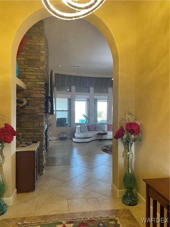 hallway with arched walkways, light tile patterned flooring, and baseboards