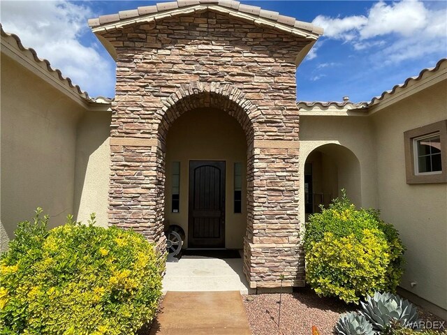 view of exterior entry featuring stone siding, a tile roof, and stucco siding