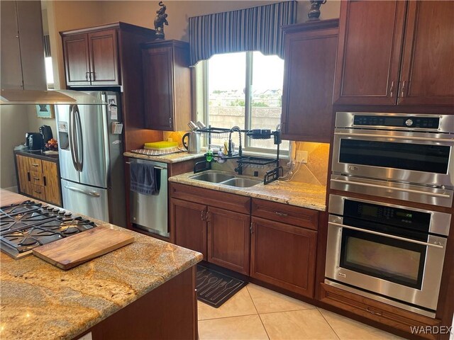 kitchen with light stone counters, stainless steel appliances, a sink, and exhaust hood