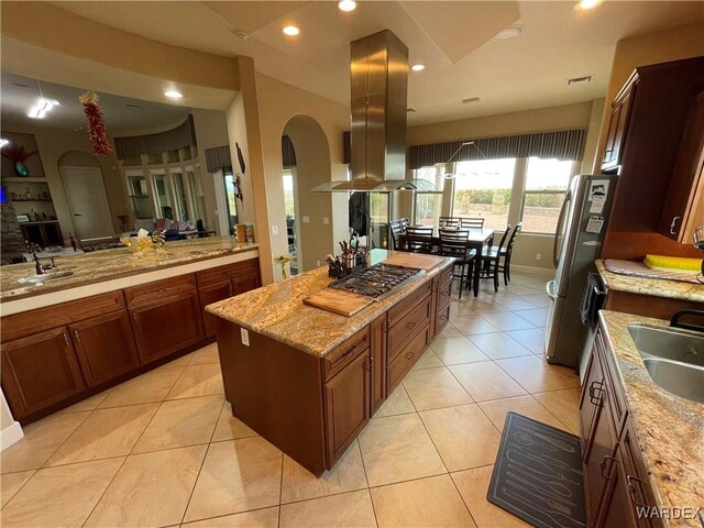 kitchen featuring light tile patterned floors, stainless steel appliances, a sink, island range hood, and light stone countertops