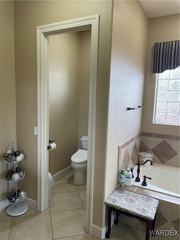 bathroom featuring toilet, a garden tub, baseboards, and tile patterned floors