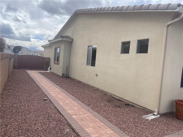 view of side of home featuring a tile roof, fence, a patio, and stucco siding