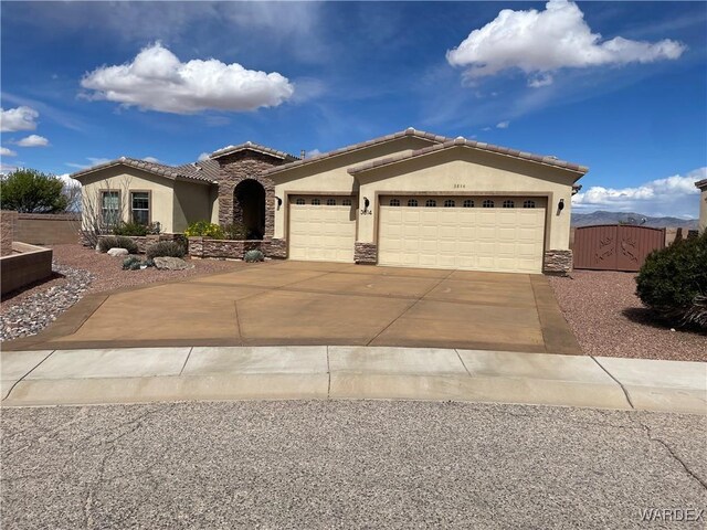 mediterranean / spanish house featuring an attached garage, stone siding, driveway, a gate, and stucco siding