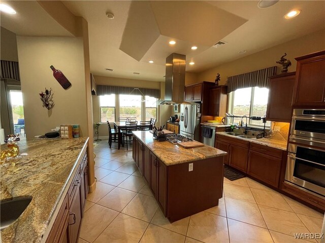 kitchen featuring island range hood, appliances with stainless steel finishes, a center island, light stone countertops, and a sink