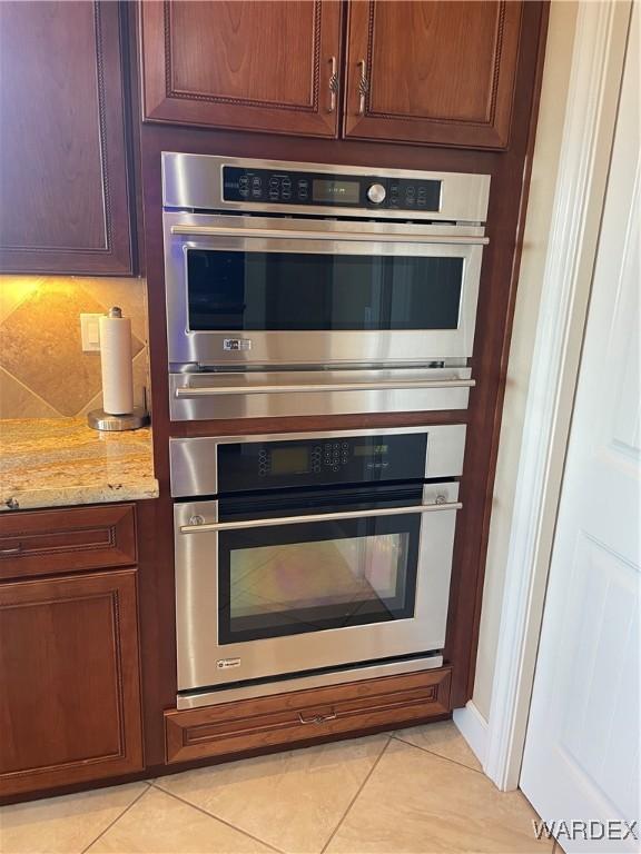 kitchen with light tile patterned floors, double oven, light stone counters, and backsplash