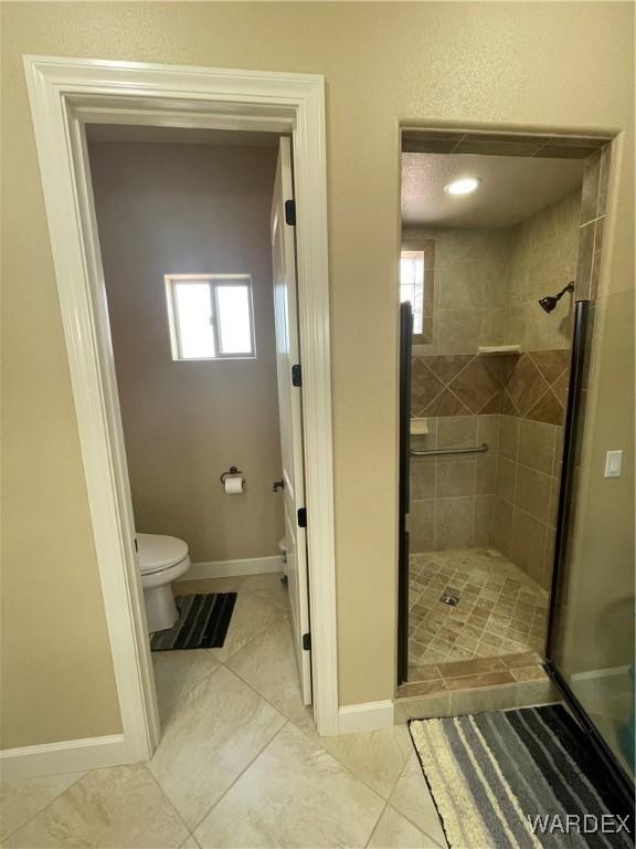 full bathroom featuring toilet, a stall shower, and baseboards