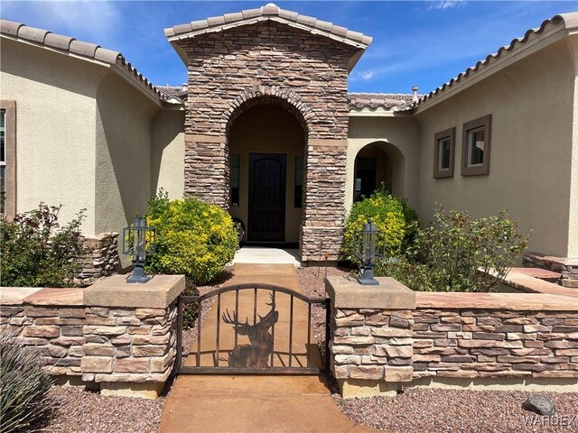 doorway to property featuring stone siding, a tile roof, a gate, and stucco siding