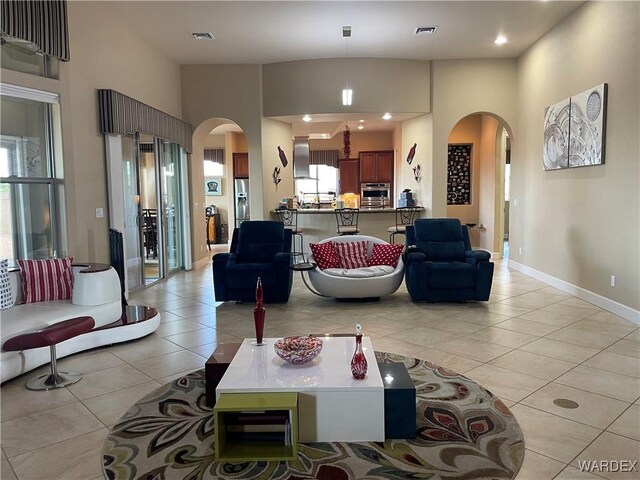 living room featuring arched walkways, light tile patterned floors, visible vents, and baseboards