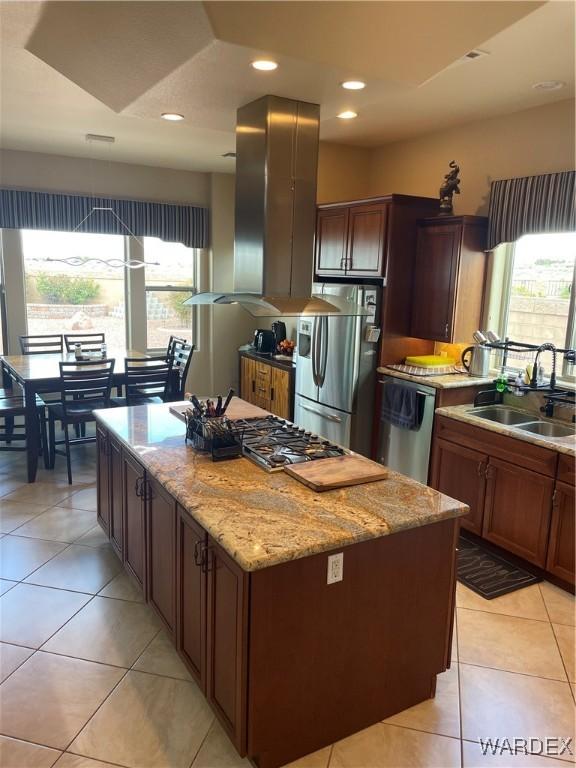 kitchen featuring light tile patterned floors, stainless steel appliances, a kitchen island, a sink, and light stone countertops