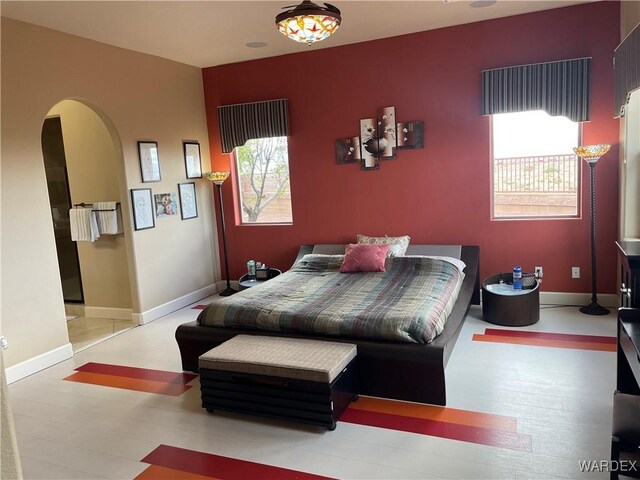 bedroom with light wood-style floors, baseboards, and arched walkways