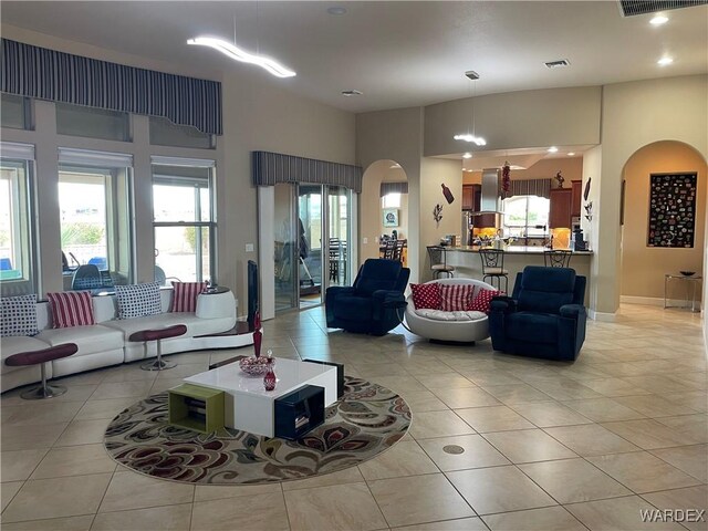 living area with arched walkways, light tile patterned floors, recessed lighting, visible vents, and baseboards