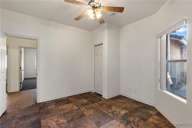 unfurnished bedroom with stone finish flooring, a closet, baseboards, and a ceiling fan