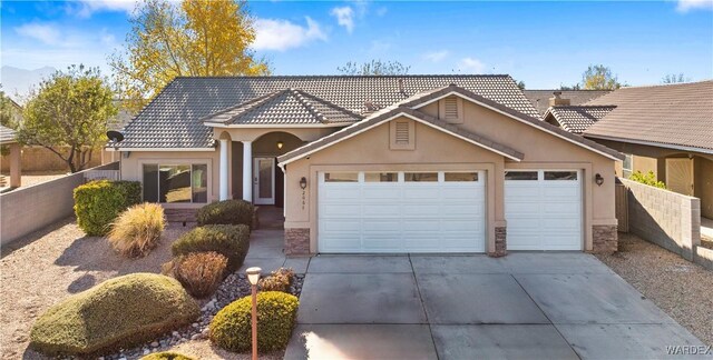 view of front of house with concrete driveway, stone siding, an attached garage, fence, and stucco siding