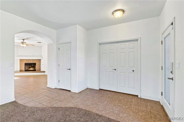 unfurnished bedroom with arched walkways, light tile patterned floors, a fireplace, and baseboards