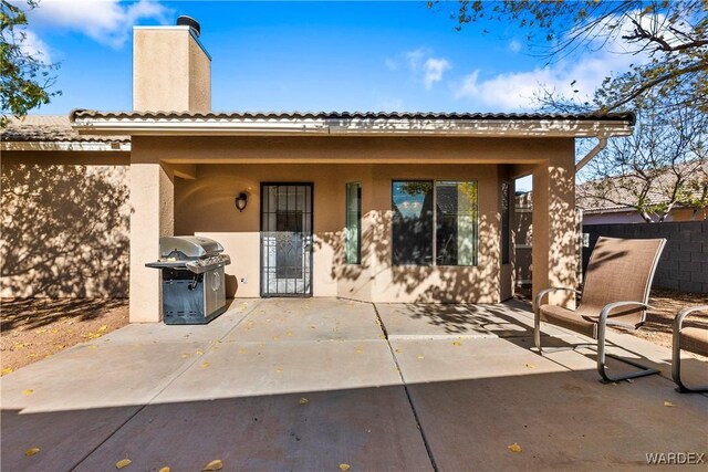 back of house with stucco siding, a chimney, fence, and a patio