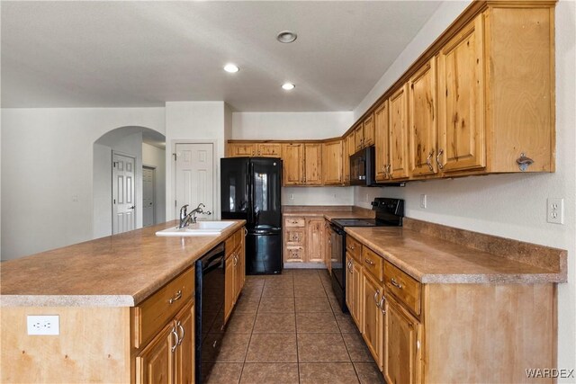 kitchen with arched walkways, dark tile patterned floors, a sink, black appliances, and an island with sink