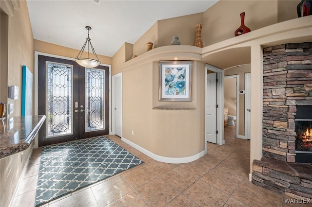 foyer entrance featuring french doors, a stone fireplace, baseboards, and tile patterned floors