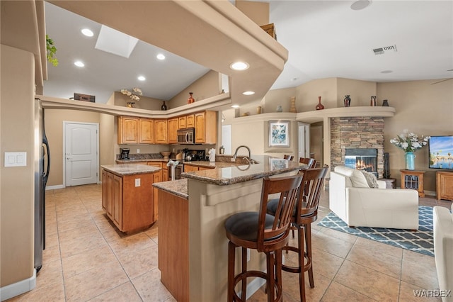 kitchen featuring light stone counters, visible vents, appliances with stainless steel finishes, open floor plan, and an island with sink