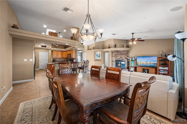 dining area with light tile patterned floors, visible vents, lofted ceiling, a stone fireplace, and ceiling fan with notable chandelier