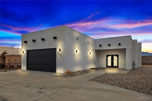 pueblo-style house with fence, driveway, stucco siding, french doors, and a garage