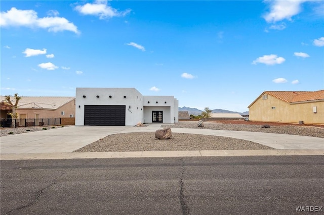 adobe home featuring stucco siding, driveway, an attached garage, and fence