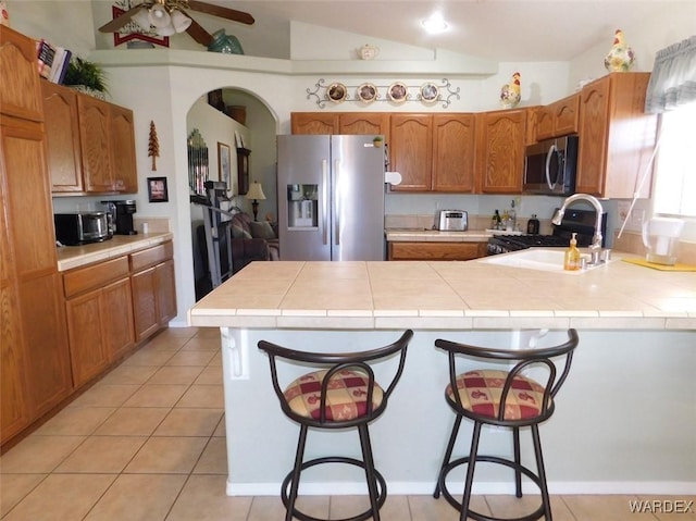 kitchen with a peninsula, a kitchen bar, appliances with stainless steel finishes, and tile countertops