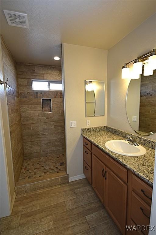 bathroom featuring visible vents, a tile shower, vanity, and wood finished floors