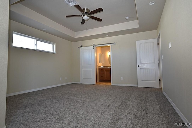 unfurnished bedroom featuring a tray ceiling, baseboards, carpet, and a barn door