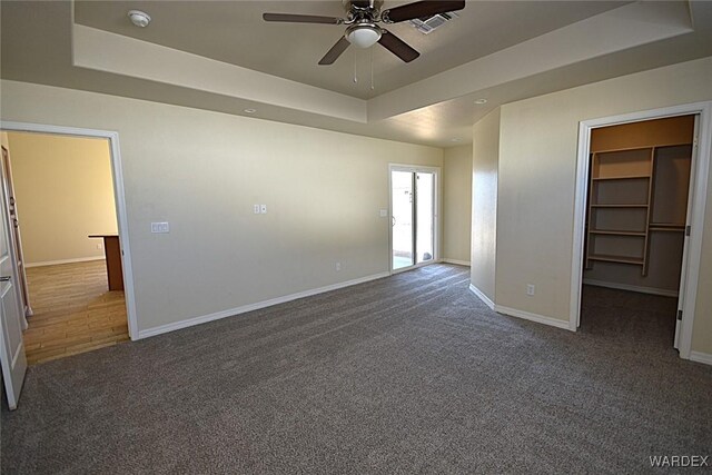 unfurnished bedroom with carpet floors, a tray ceiling, a walk in closet, and baseboards