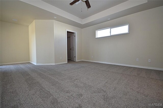 carpeted empty room featuring ceiling fan, baseboards, and a raised ceiling