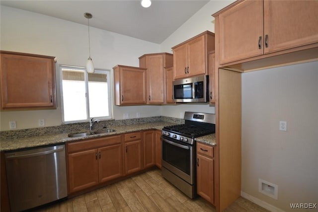 kitchen with decorative light fixtures, light wood finished floors, stainless steel appliances, a sink, and light stone countertops