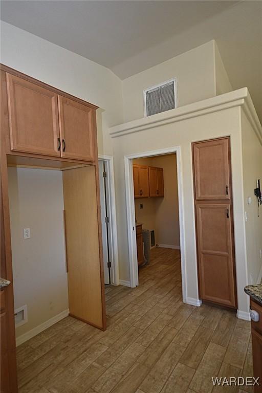 interior space featuring lofted ceiling, light wood-type flooring, visible vents, and baseboards