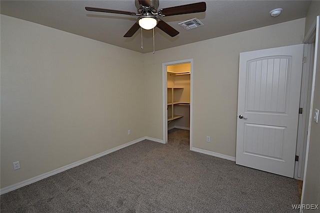 unfurnished bedroom with ceiling fan, visible vents, baseboards, dark colored carpet, and a walk in closet